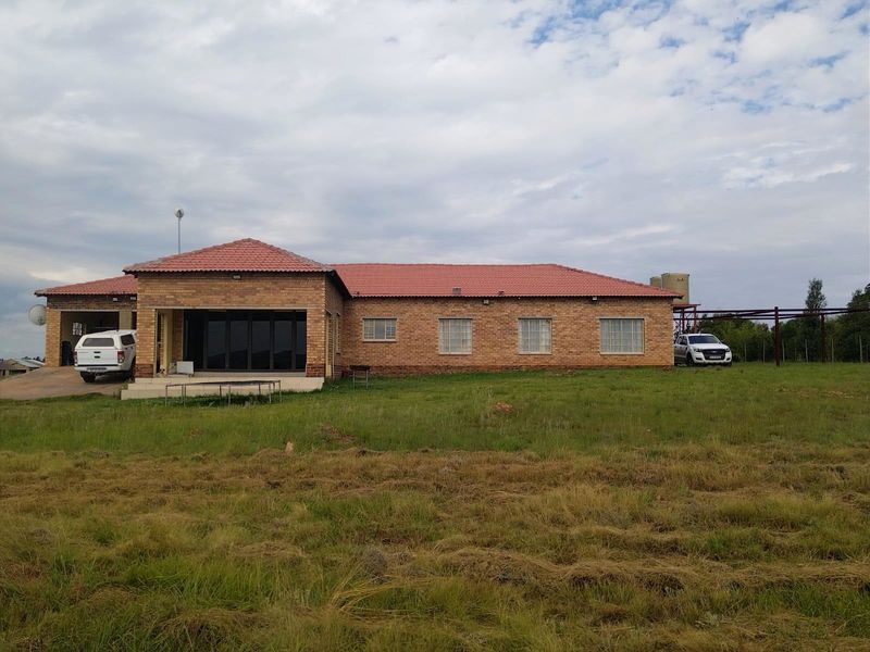 Rear view of a single-story face brick farmhouse featuring a tiled roof, covered patio area, and integrated water storage tanks on a large plot.