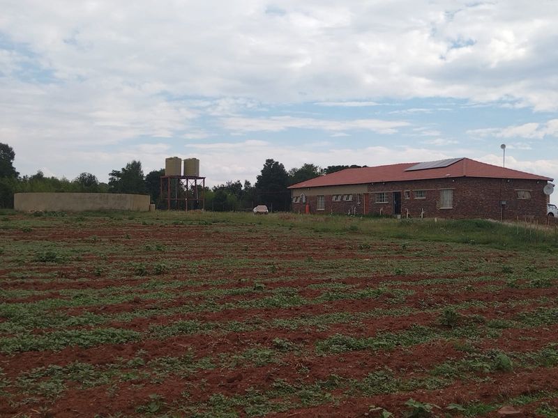 A view of the farm property featuring a brick building with a tiled roof, solar panels, water storage tanks, and a concrete reservoir.