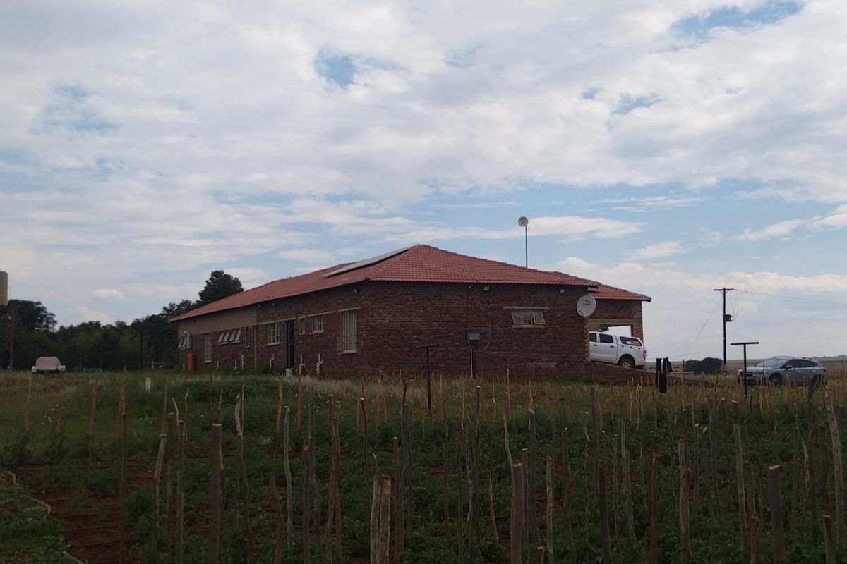 A rear view of a brick farmhouse featuring a tiled roof with solar panels, set against a rural landscape.