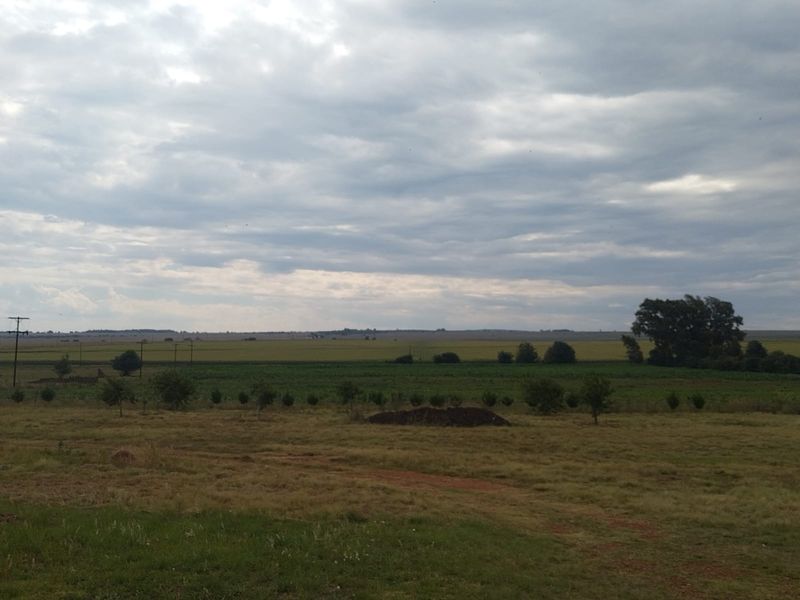 A wide-angle view of the expansive farm landscape featuring open fields and natural vegetation under a cloudy sky.
