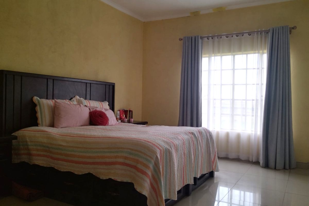 A spacious bedroom featuring tiled flooring, a large grid-pattern window with curtains, and yellow-toned walls with some visible surface wear.