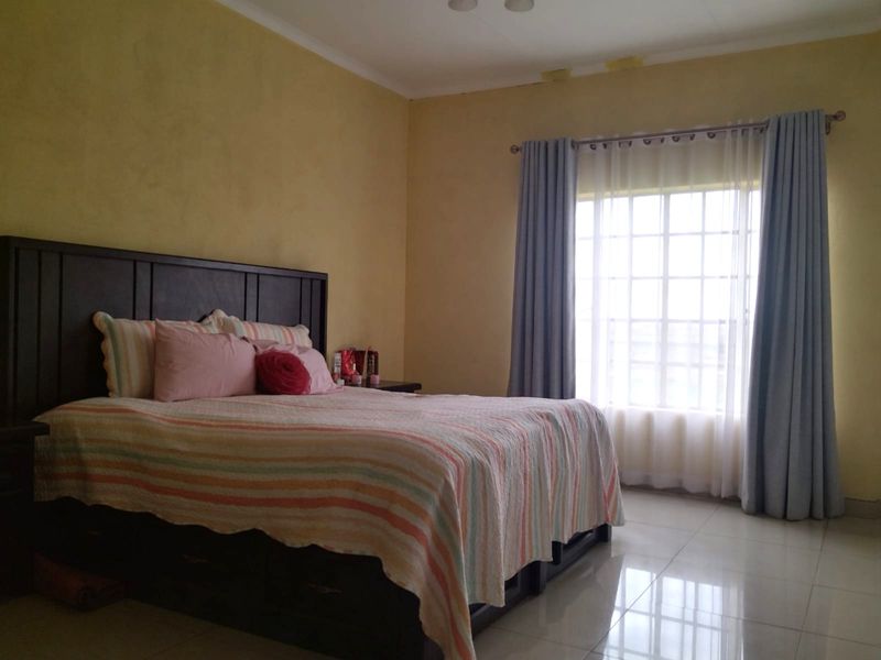 A spacious bedroom featuring tiled flooring, a large grid-pattern window with curtains, and yellow-toned walls with some visible surface wear.