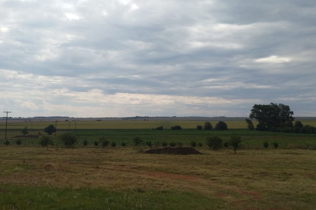 A wide-angle view of the expansive farm landscape featuring open fields and natural vegetation under a cloudy sky.
