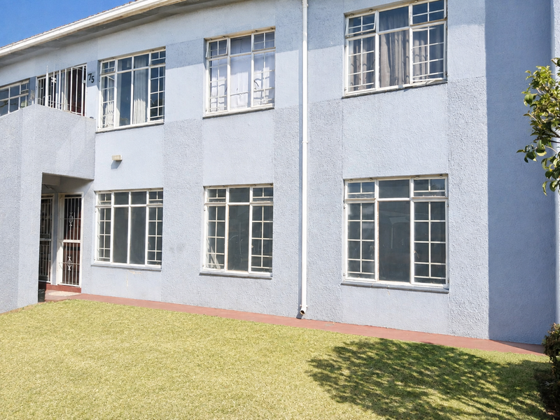 Front elevation of a multi-story apartment building featuring textured blue plaster, steel-framed windows, and security gates at the entrance.