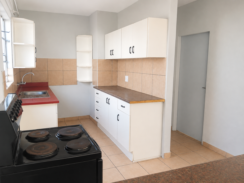 A functional kitchen featuring white cabinetry, laminate countertops, tiled backsplash, and a freestanding electric stove with tiled flooring.