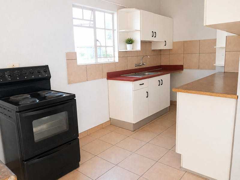A functional kitchen featuring white cabinetry, laminate countertops, tiled splashbacks, and a freestanding stove, offering a clean and practical workspace.