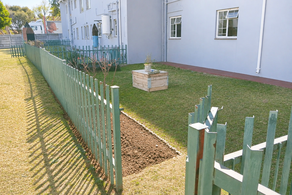 Rear exterior view of the apartment building featuring a lawn area, paved walkway, and metal palisade fencing.