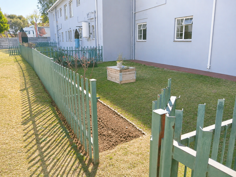 Rear exterior view of the apartment building featuring a lawn area, paved walkway, and metal palisade fencing.