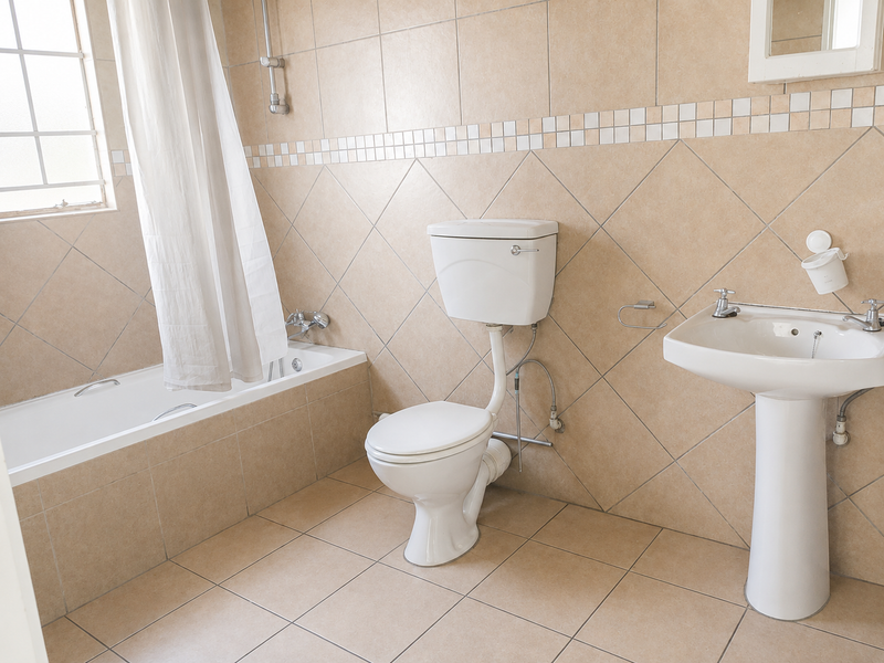 A functional bathroom featuring a bathtub, pedestal basin, and toilet with neutral ceramic wall and floor tiling.
