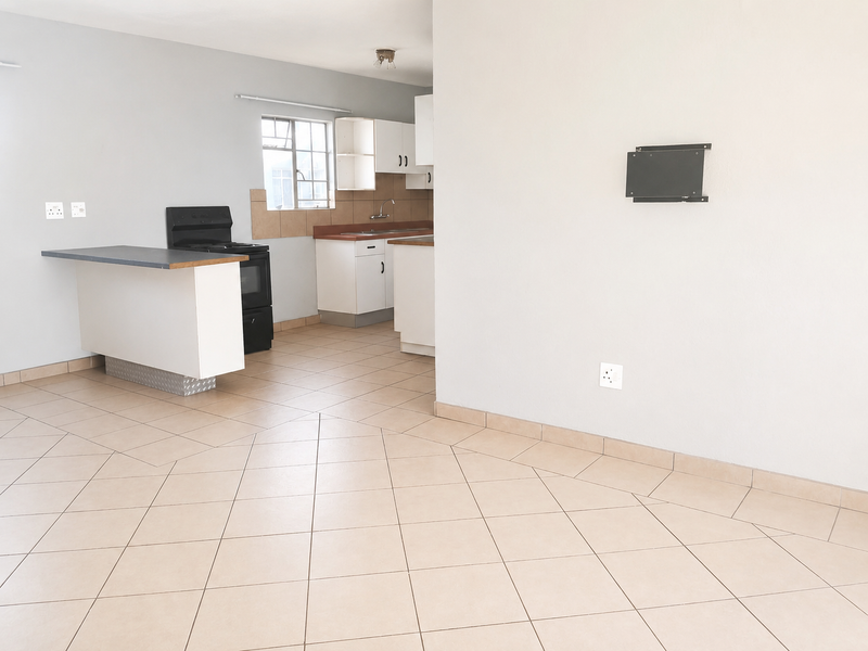 An open-plan living and kitchen area featuring tiled flooring, built-in cabinetry, a breakfast counter, and a freestanding stove in a neutral, vacant space.