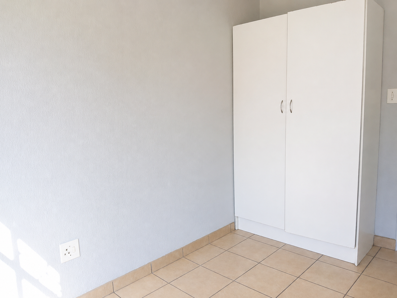 A clean, empty bedroom featuring neutral wall paint, tiled flooring, and a functional built-in white wardrobe.
