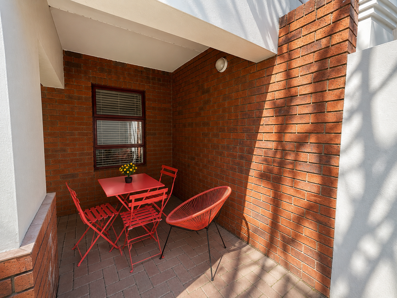 A covered patio area featuring exposed brick walls and paved flooring, providing a private outdoor space for relaxation.