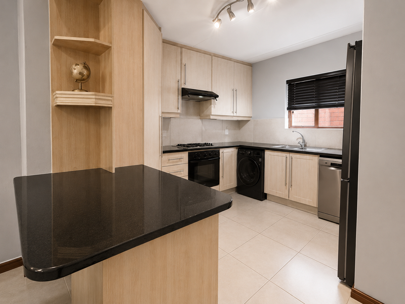 Modern kitchen featuring light wood cabinetry, black granite countertops, built-in appliances, and tiled flooring with a breakfast bar area.