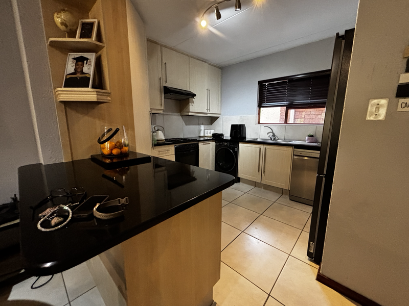 A functional kitchen featuring light wood cabinetry, black granite countertops, tiled flooring, and integrated appliances, offering a practical layout for daily use.