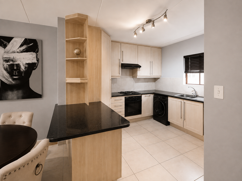 Modern kitchen featuring light wood cabinetry, black granite countertops, integrated gas hob, oven, and tiled flooring with a functional breakfast bar layout.