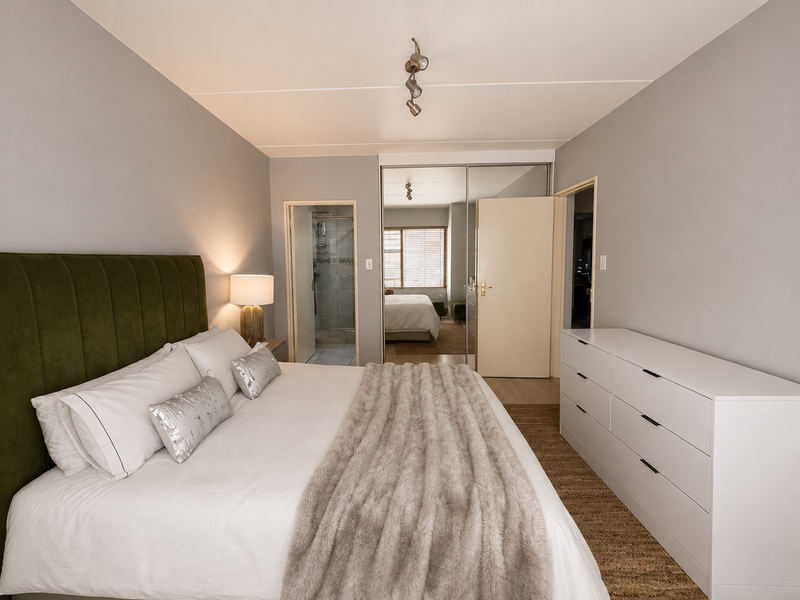 A well-maintained bedroom featuring built-in wardrobes with mirrored sliding doors, track lighting, and an adjoining en-suite bathroom.