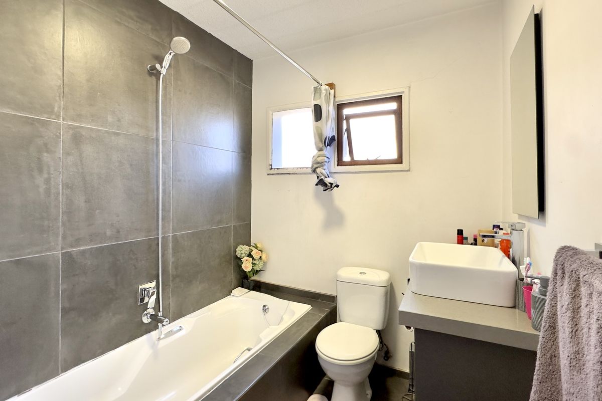 A functional bathroom featuring a built-in bathtub with grey tiled surround, a modern vessel sink on a vanity, and a standard toilet.