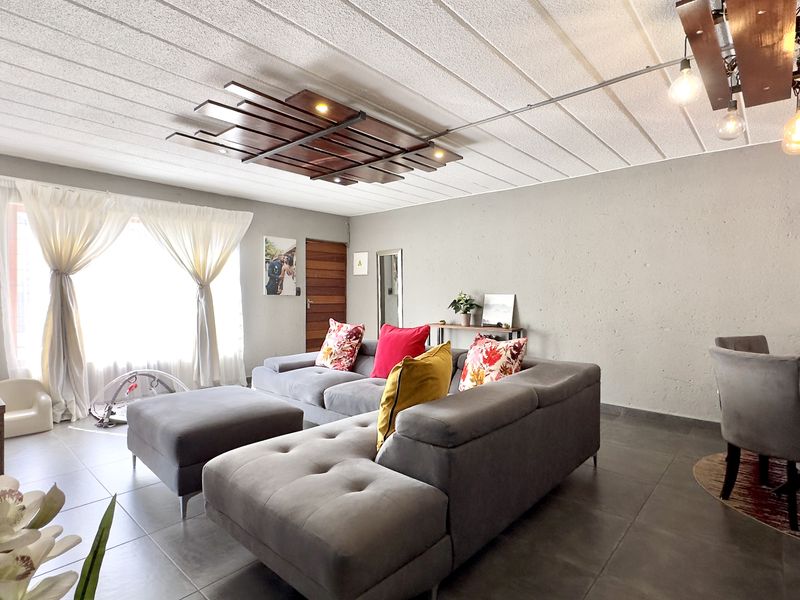 An open-plan living and dining area featuring tiled flooring, a textured ceiling with decorative lighting, and neutral wall finishes.