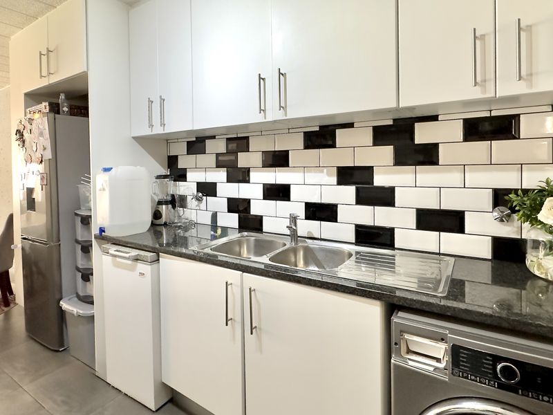 A functional kitchen featuring white cabinetry, a contrasting black and white subway tile backsplash, granite countertops, and a double stainless steel sink.