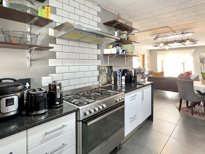 Modern open-plan kitchen and living area featuring a gas stove, subway tile backsplash, granite countertops, and industrial-style exposed ceiling lighting.