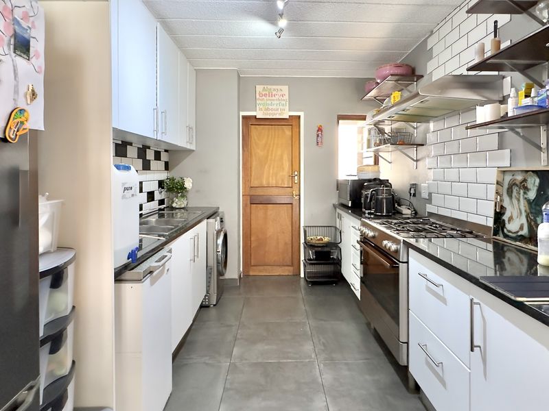 A functional galley-style kitchen featuring white cabinetry, granite countertops, a gas hob with extractor, and modern subway tile backsplash.