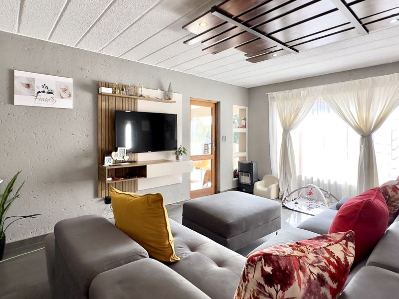 A well-maintained living room featuring a decorative ceiling design, built-in media cabinetry, tiled flooring, and natural light through a large window.