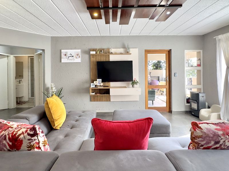 Spacious living room featuring a modern built-in media unit, unique timber ceiling detail, and direct access to an outdoor patio area.