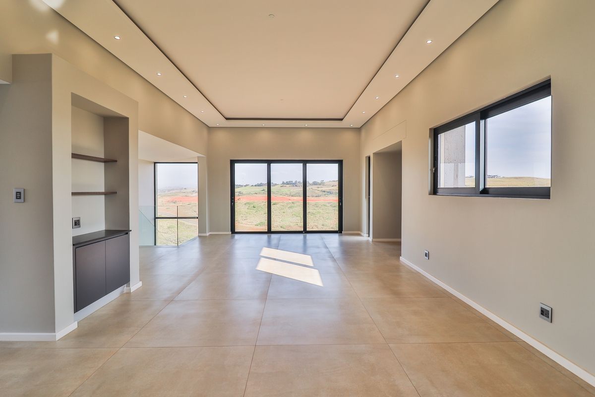 Spacious, modern open-plan living area featuring large sliding glass doors, neutral tiled flooring, recessed tray ceiling lighting, and built-in cabinetry with scenic views.