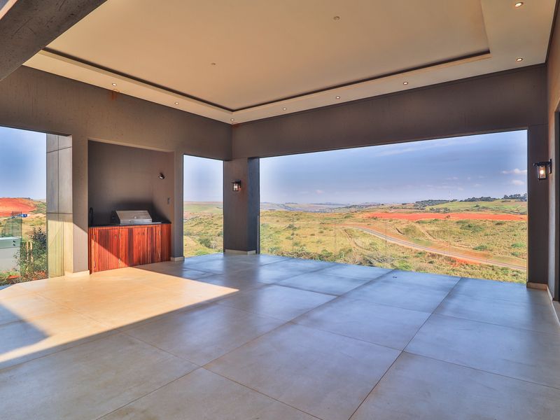Spacious covered patio featuring a built-in braai, glass balustrade, and expansive panoramic views of the surrounding landscape.