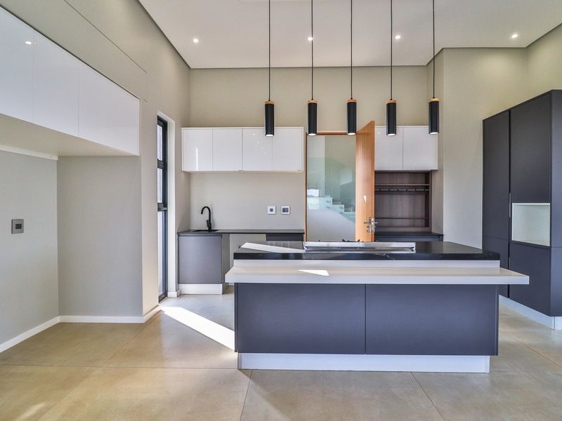 Modern kitchen featuring a central island, sleek two-tone cabinetry, stone countertops, and contemporary pendant lighting in a spacious, well-lit layout.