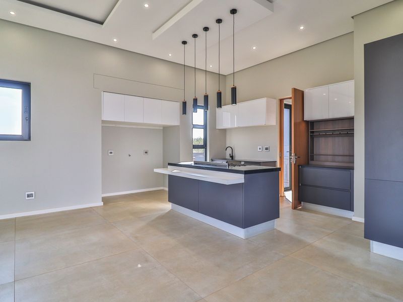 Modern, spacious kitchen featuring a central island, sleek cabinetry, stone countertops, and contemporary pendant lighting in an open-plan layout.
