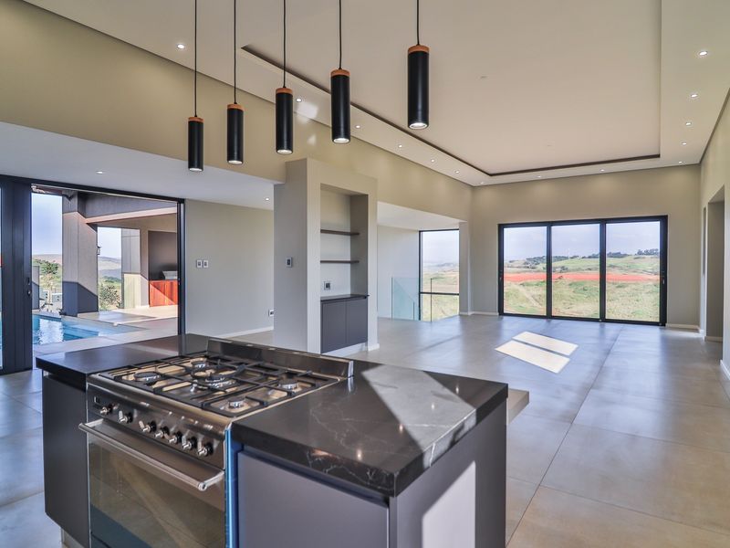 Spacious open-plan living area featuring a modern kitchen island with gas stove, sleek tiled flooring, and large sliding doors opening to the pool area.