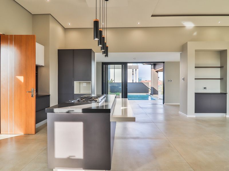 Modern open-plan kitchen featuring a central island with gas cooktop, sleek cabinetry, and seamless flow to an outdoor patio and pool area.