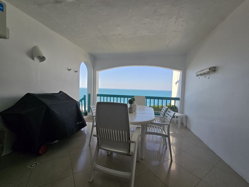 A covered balcony featuring tiled flooring, a protective balustrade, and an arched opening with expansive ocean views.