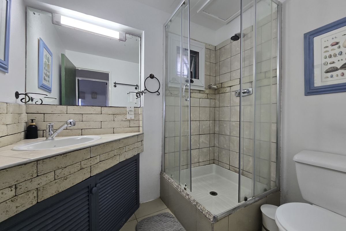 A functional bathroom featuring a shower enclosure, vanity with integrated sink, and tiled finishes, offering potential for a modern cosmetic update.
