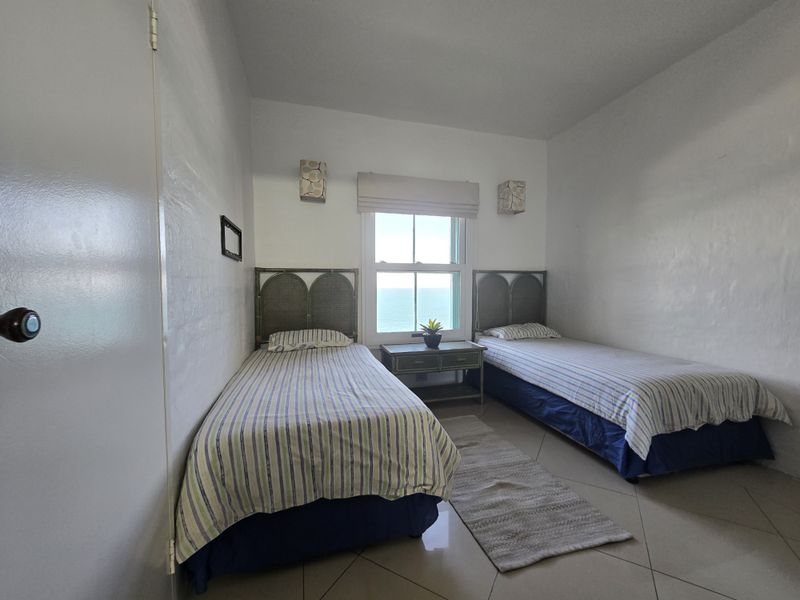 A bedroom featuring tiled flooring, wall-mounted light fixtures, and a sash window with a view of the ocean.