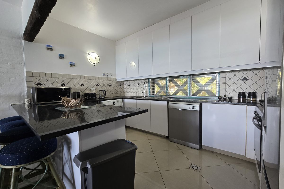 Modern kitchen featuring sleek white cabinetry, dark granite countertops, a tiled backsplash, and integrated stainless steel appliances, offering a clean and functional workspace.