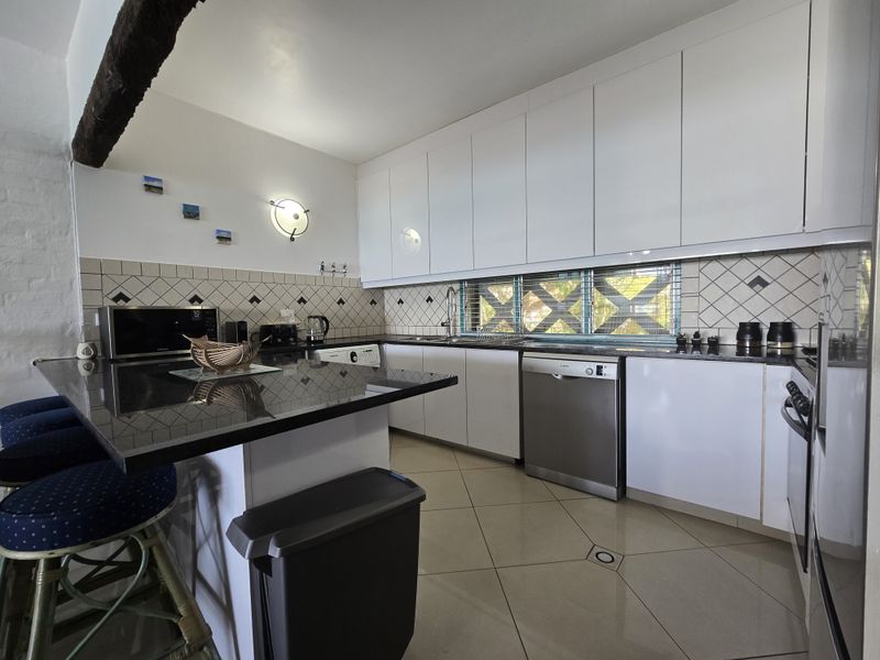 Modern kitchen featuring sleek white cabinetry, dark granite countertops, a tiled backsplash, and integrated stainless steel appliances, offering a clean and functional workspace.