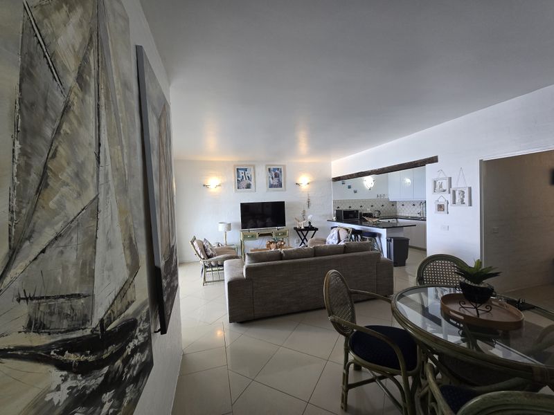 Open-plan living and kitchen area featuring tiled flooring, neutral walls, and a breakfast bar, creating a functional and connected living space.
