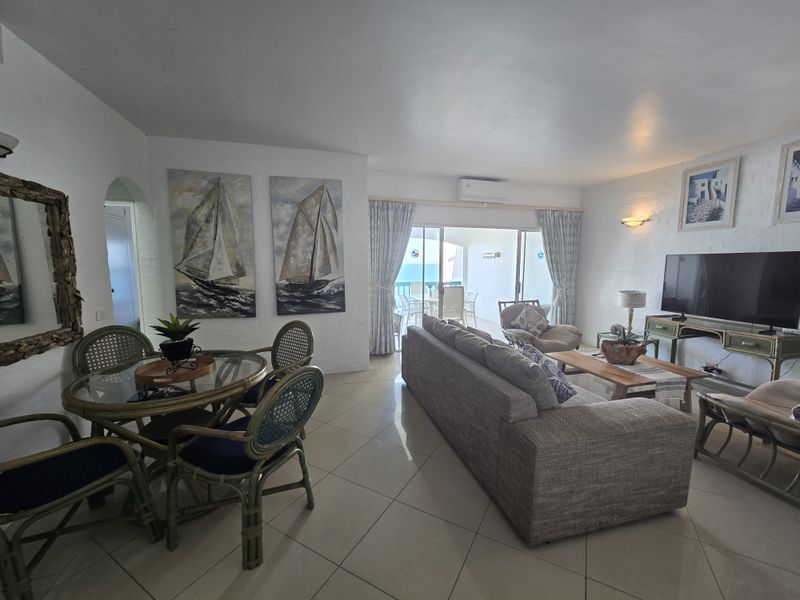 Open-plan living and dining area featuring tiled floors, wall-mounted air conditioning, and large sliding doors leading to a balcony with ocean views.
