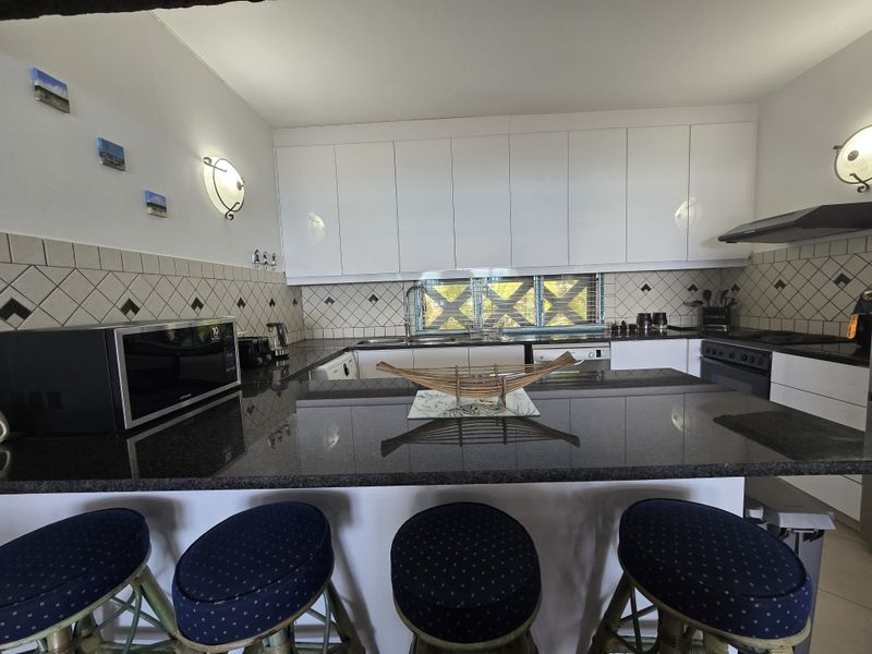 A well-maintained kitchen featuring granite countertops, white cabinetry, a tiled backsplash, and integrated appliances including an oven and extractor fan.