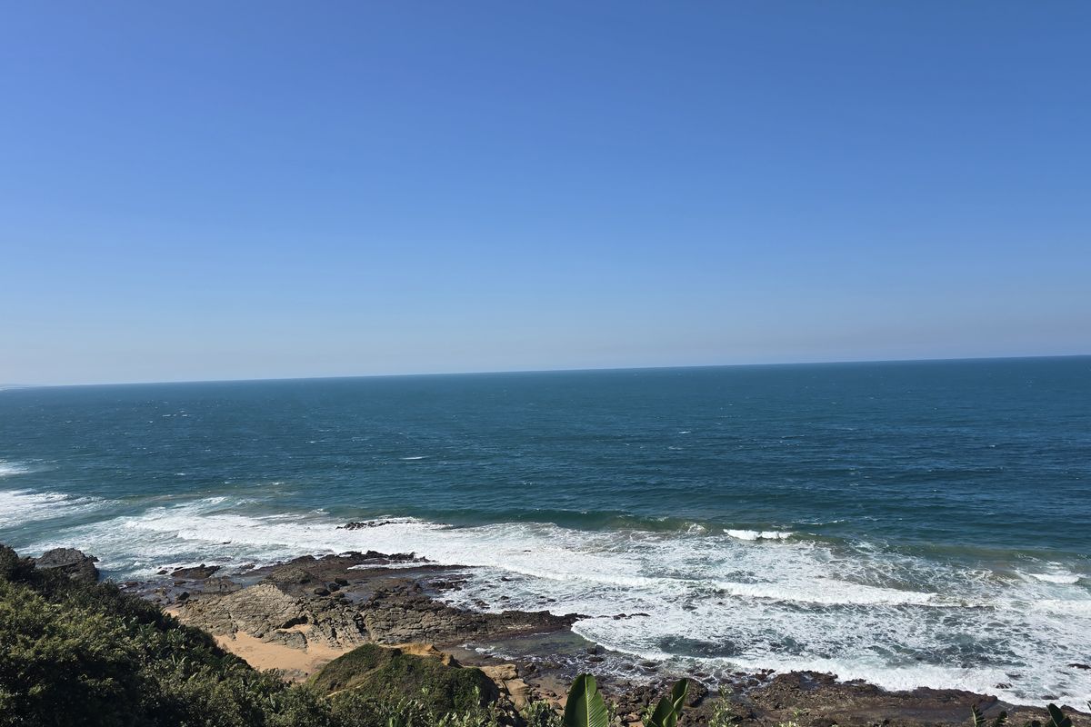 A scenic, elevated view of the ocean coastline featuring rocky shores and natural vegetation.