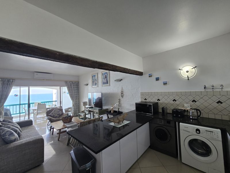 Open-plan living area featuring a modern kitchen with granite countertops, integrated laundry appliances, and seamless access to a balcony with ocean views.