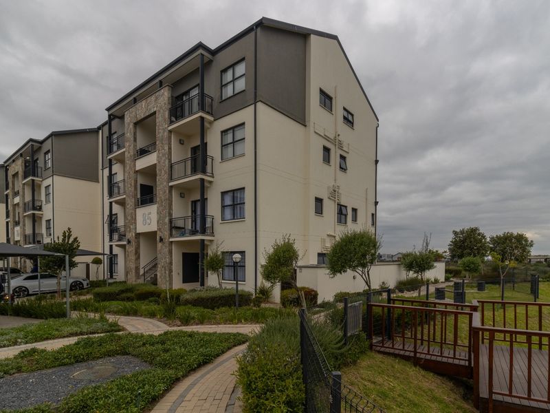 Exterior view of a modern multi-story apartment building featuring stone facade accents, private balconies, landscaped grounds, and paved walkways.