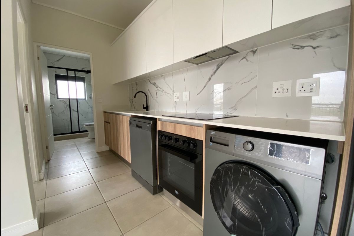 Modern kitchen featuring sleek white and wood-grain cabinetry, marble-look splashback, stone countertops, and integrated appliances, with a view into the adjacent bathroom.