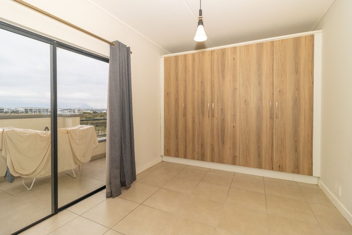 A bright, empty bedroom featuring modern wood-finish built-in cupboards, tiled flooring, and a sliding glass door leading to a private balcony.