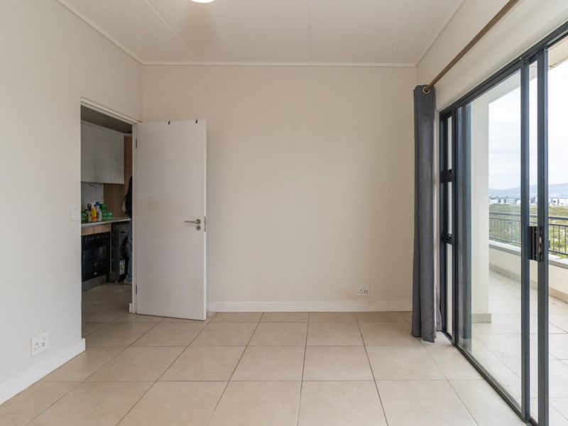 An empty, well-lit living area featuring neutral tiled flooring and a large sliding glass door providing access to an outdoor balcony.