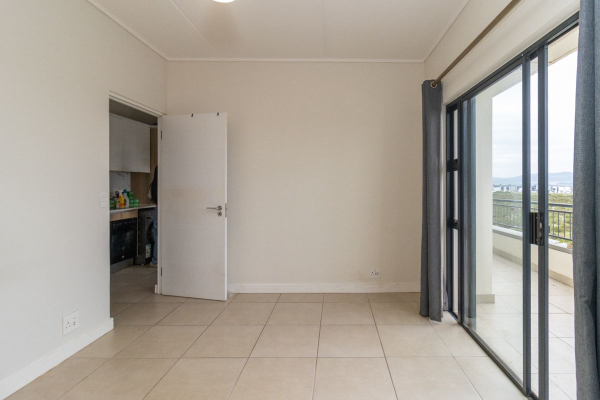 An empty, well-lit living area featuring neutral tiled flooring and a large sliding glass door providing access to an outdoor balcony.