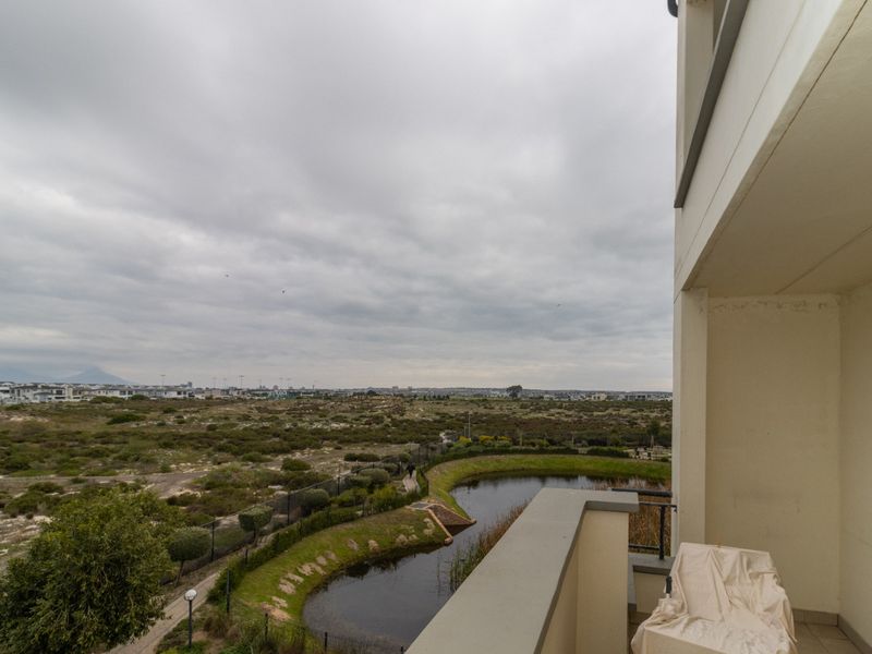A private balcony featuring tiled flooring and a metal railing, offering expansive views over the surrounding landscape and natural pond area.