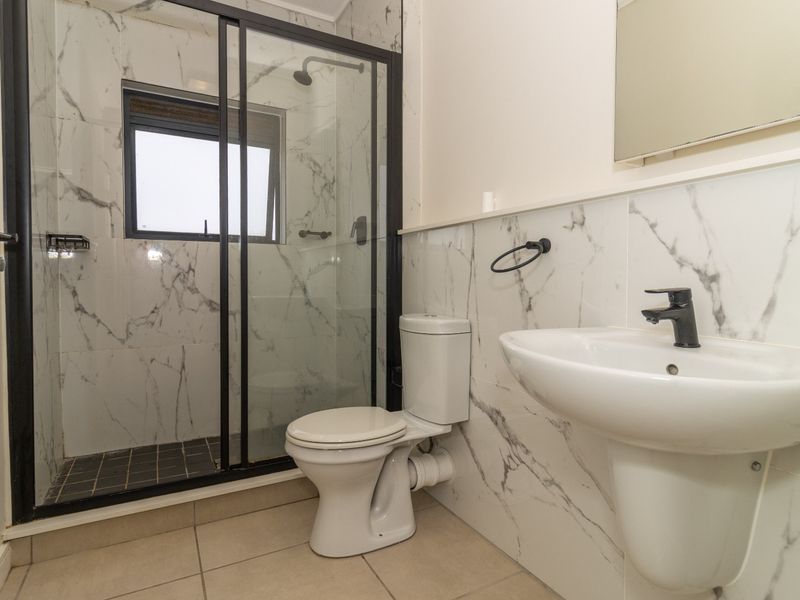 Modern bathroom featuring a walk-in shower with black-framed glass enclosure, marble-look wall tiling, pedestal basin, and contemporary black fixtures.